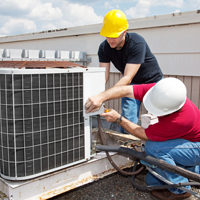 Two workers on the roof of a building working on the air conditioning unit.