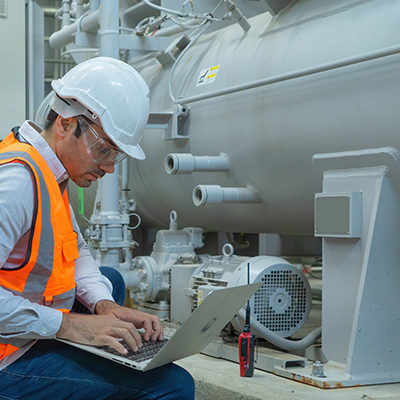 man kneeling with computer on lap next to a storage tank