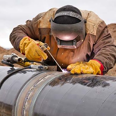 man with welding helmet, gloves and a torch welding a large natural gas transmission pipe